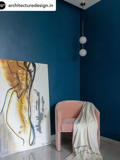 A reading corner that combines bold color and soft textures. A deep blue wall serves as a dramatic backdrop for a plush pink chair and abstract art, creating a perfect spot for quiet reflection.