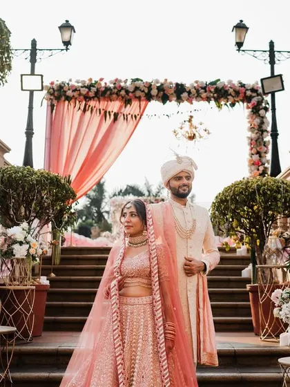 A beautiful portrait of the couple on the steps of a grand venue. The pastel colors of their outfits and the floral decor create a soft and romantic scene.