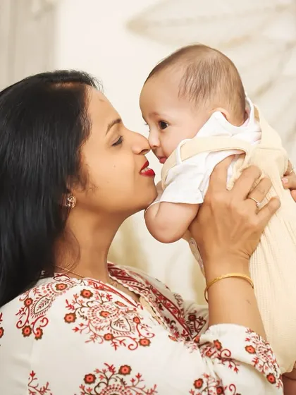 A beautiful, intimate moment between a mother and her baby. She leans in for a kiss, her face full of love, in a softly lit studio setting.
