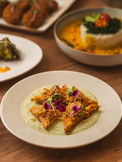 Artfully plated samosas on a bed of green sauce, garnished with edible flowers. This image elevates a classic street food into a gourmet appetizer through careful food styling and photography.