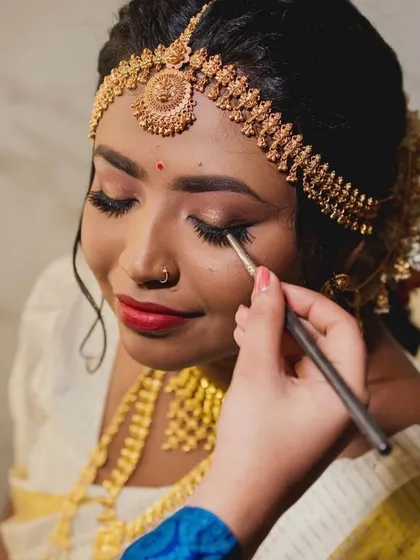 A close-up moment of applying the final touches of eye makeup for this beautiful Kerala bride, enhancing her features for her special day.