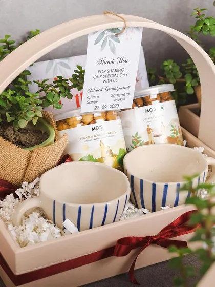 A beautiful and bougie thank you hamper for a special event. This gift includes hand-painted ceramic mugs, gourmet snacks, and a live plant, all presented in an elegant basket.