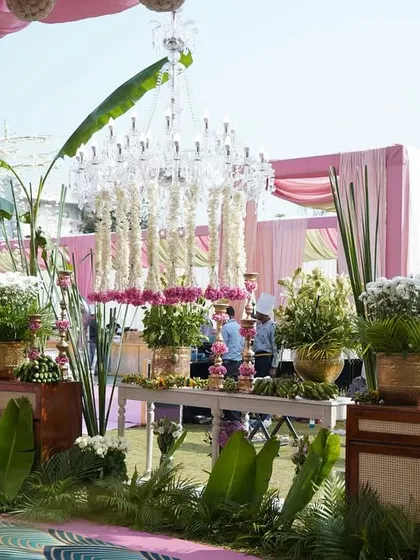 A decor setup featuring floral arrangements, traditional garlands, and elegant chandeliers made of white flowers. The use of fresh banana leaves as a base adds a wonderful natural element.