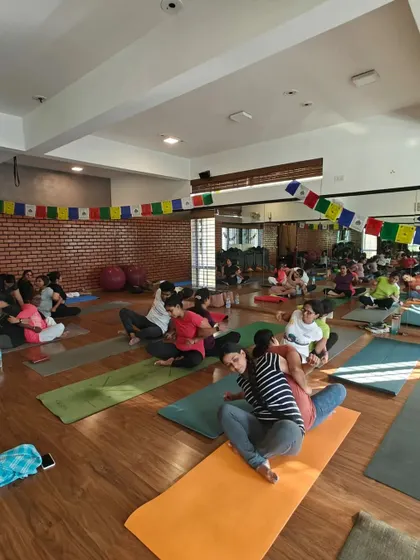 A wide view of the partner yoga workshop, where pairs are working together in various stages of their practice. The sense of community and shared learning is palpable.