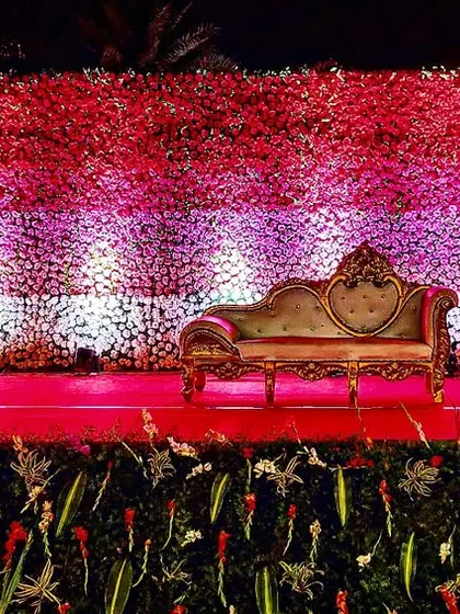 A wide view of a wedding reception backdrop, showcasing a vibrant wall of red, pink, and white flowers. This kind of floral wall creates a dramatic and colorful setting for any celebration.