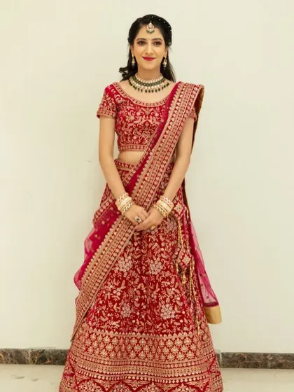 A full-length view of the stunning bride in her red reception lehenga. The pink and gold glitter eye makeup beautifully ties in with the intricate embroidery of her outfit, creating a cohesive and regal bridal look.