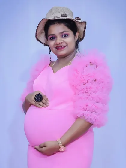 A chic maternity look, with the mother-to-be in a pink ruffled gown accessorized with a stylish hat.