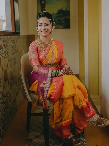 A full-length seated portrait of the bride, showcasing the beautiful drape of her Nauvari saree and her elegant pose.