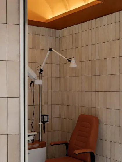 Even functional areas like the vision assessment room are designed with care, featuring the same warm material palette of neutral wall tiles and an arched ceiling to ensure a cohesive aesthetic throughout the store.