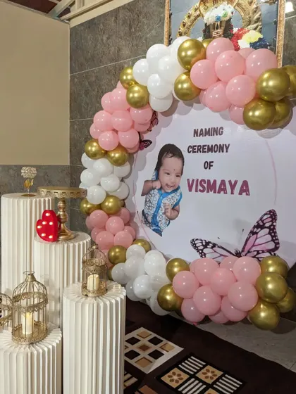 A clear shot of a modern naming ceremony setup. The pink, white, and gold balloon arch frames a custom circular backdrop, creating a perfect spot for photos.