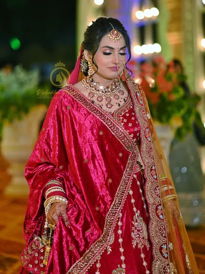 A full-length view of a stunning rani pink velvet lehenga. The way the second dupatta is draped adds a layer of elegance, and the intricate embroidery shines under the lights, making it perfect for your grand entrance.