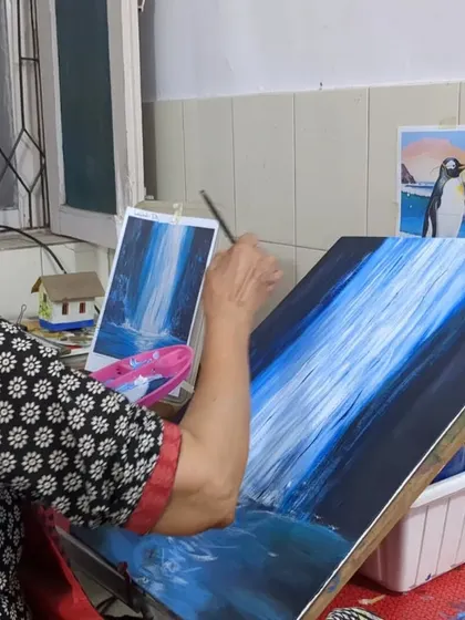 Deep in focus, Harinder ma'am meticulously works on the details of her waterfall painting, using a reference photo to guide her brushstrokes.