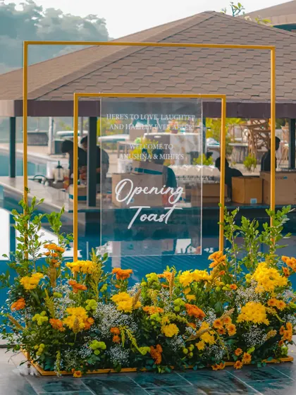 A welcome sign for the "Opening Toast" at a pre-wedding event, featuring a clear acrylic sign with elegant calligraphy, framed by yellow flowers.