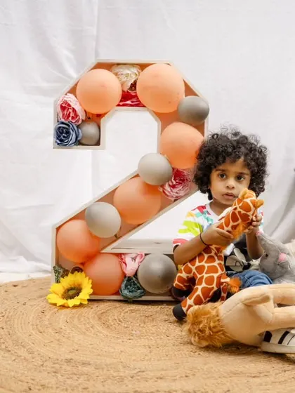 A toddler boy sits with his stuffed animals next to a "2" prop for his second birthday shoot in the park.