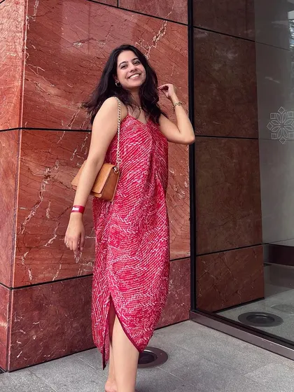 A smiling client wears her custom-made pleated pink asymmetric dress. This design is perfect for someone looking for a contemporary and comfortable yet eye-catching outfit.