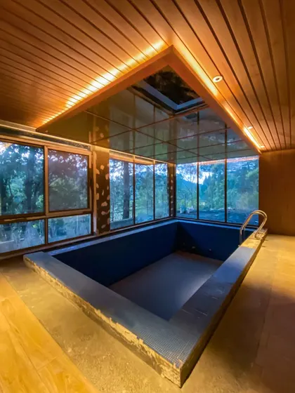An evening view of the indoor pool area under construction. The warm interior lighting contrasts beautifully with the twilight sky, showcasing the space as a year-round retreat.