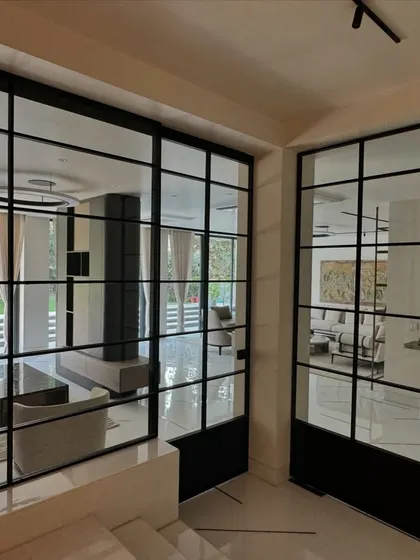 This view shows the use of black-framed glass partitions to create a sense of openness while defining different zones. This feature allows light to flow through the space and offers glimpses of the living areas and the garden beyond.