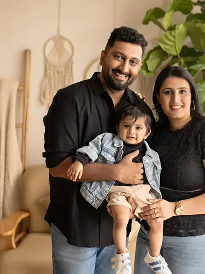 A stylish family portrait. The parents are holding their son, who is dressed in a cool denim jacket, and they all look happy and confident.