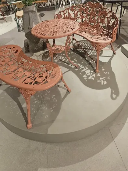 A modern take on classic cast-iron furniture. This beautiful set, with its intricate design and contemporary color, is displayed on a platform in our showroom.
