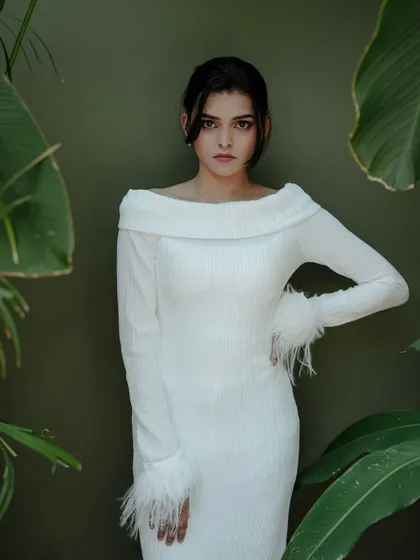 A strong and elegant pose against a simple green background. The feathered cuffs on the white dress are a beautiful detail that the clean composition highlights.