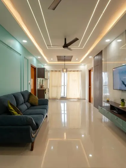 A long, spacious living room featuring a striking teal accent wall with elegant molding, a deep blue sofa, and a contemporary TV unit, all tied together by sophisticated ceiling lighting.