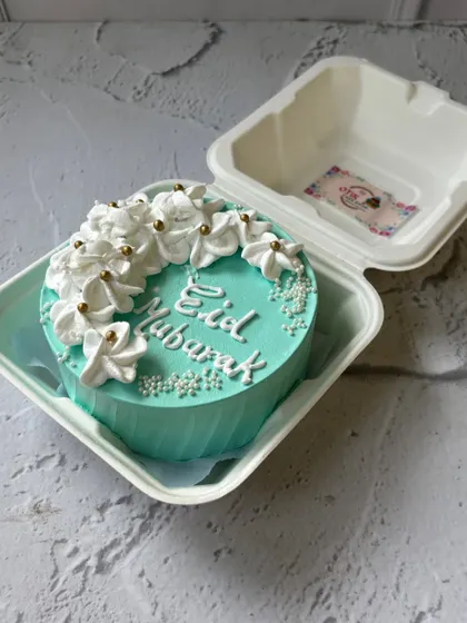 A beautiful turquoise Eid Mubarak bento cake, adorned with delicate white buttercream flowers and gold sprinkles for an elegant touch.