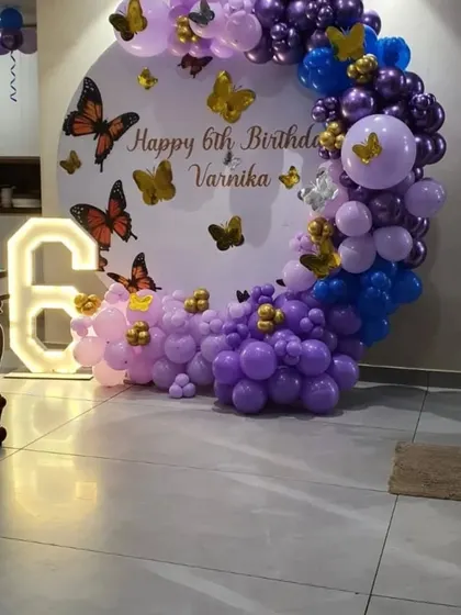A circular backdrop decorated with purple, blue, and gold balloons for a 6th birthday with a butterfly theme.