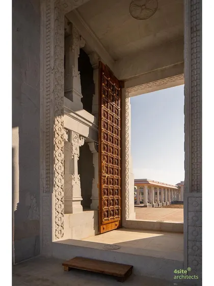 A view through the intricately carved stone doorway (*gopura dwar*) of the main shrine. The massive, detailed wooden door contrasts with the cool stone, framing the temple street beyond.