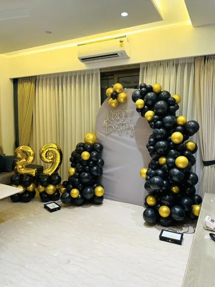 A classic black and gold 29th birthday setup with a fabric backdrop and balloon arch.