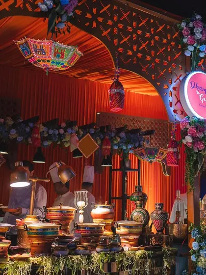 A vibrant and colourful food stall setup for a festive event. The decor, with its traditional umbrellas and floral garlands, complements the rich Indian cuisine being served.
