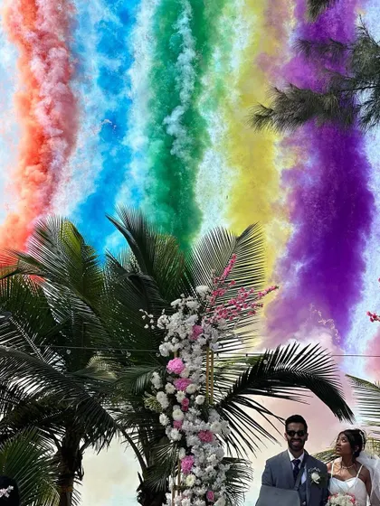 The rainbow of colors from the smoke bombs creates a stunning visual contrast with the blue sky and green palms of a destination wedding.