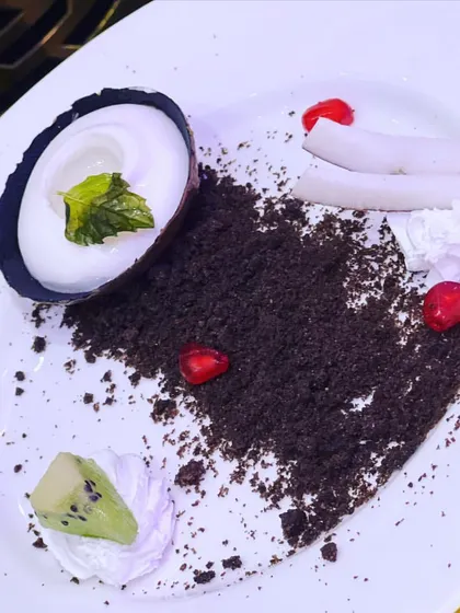 An example of my plated dessert artistry. This dish features a coconut mousse in a chocolate shell with Oreo crumble, kiwi, and pomegranate seeds, combining textures and flavors for a sophisticated dessert course.