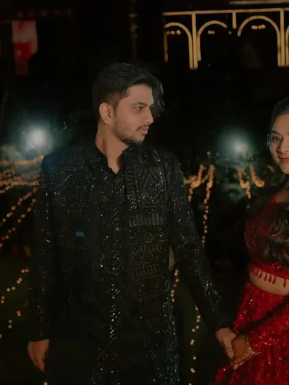 A couple holds hands against a backdrop of fairy lights, a beautiful moment from their Sangeet or reception.