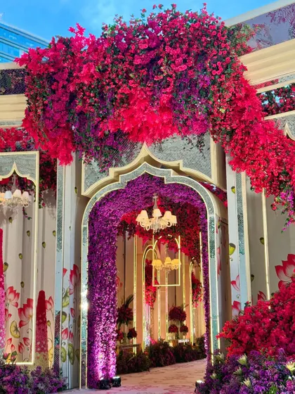 A grand entrance to a vibrant celebration. The walkway is framed by an arch of red and purple flowers, leading guests into a world of color and magic.