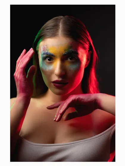 A colorful and expressive studio portrait using Holi-inspired powder for a vibrant, artistic effect. The mix of colors on the model's face and hands creates a playful yet intense image.