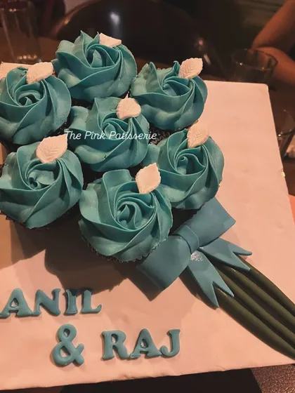 A unique and charming cupcake bouquet created for a celebration. The cupcakes are piped with teal frosting to resemble a bouquet of roses, complete with a fondant bow and stems.