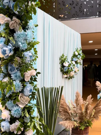 A beautiful backdrop of light blue drapes with a floral arch and wreaths, creating a serene and heavenly atmosphere for a Sai Sandhya.