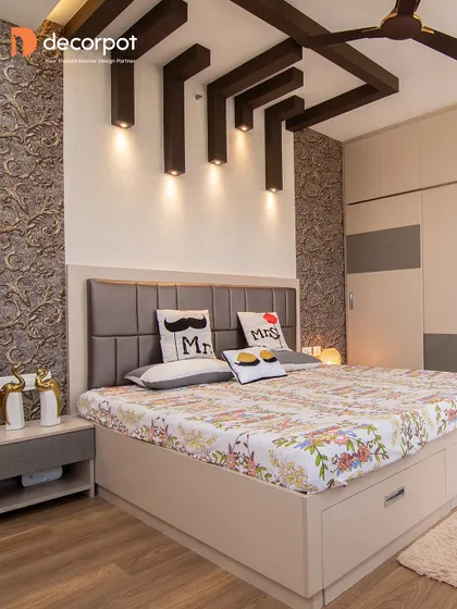 This bedroom combines textured wallpaper, a simple upholstered headboard, and unique ceiling rafters with spotlights. The result is a cozy and modern space with plenty of character.