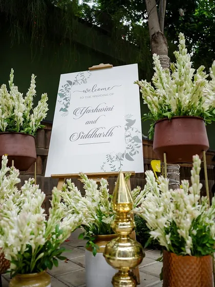 An elegant welcome setup featuring a personalized sign surrounded by fragrant tuberoses in earthy terracotta pots. The combination of rustic and refined elements creates a warm greeting.