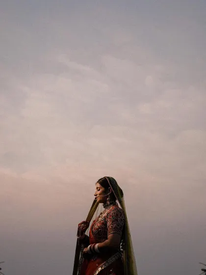 A minimalist yet powerful portrait against the sky. This shot, similar to 95, emphasizes the bride's silhouette and the color of her lehenga against the soft clouds.