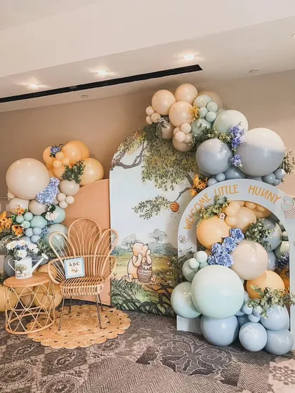 A beautiful Winnie the Pooh themed baby shower. The hand-painted style backdrop, pastel balloons, and rattan furniture create a classic and whimsical feel.