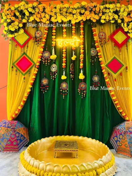 A traditional Haldi backdrop with green and yellow drapes, adorned with colorful hangings and umbrellas.