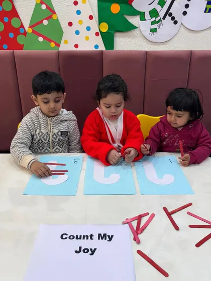 Three little learners focused on their "Count My Joy" activity. Using simple materials like craft sticks helps develop fine motor skills alongside their ability to count and recognize numbers.