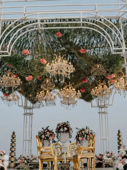 The intricate details of the mandap's floral canopy are visible here, with golden chandeliers nestled amongst a thick layer of hanging foliage and pink blooms.