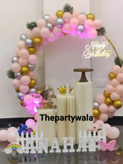 A peach, pink, and gold balloon ring with a 'Happy Birthday' neon sign.
