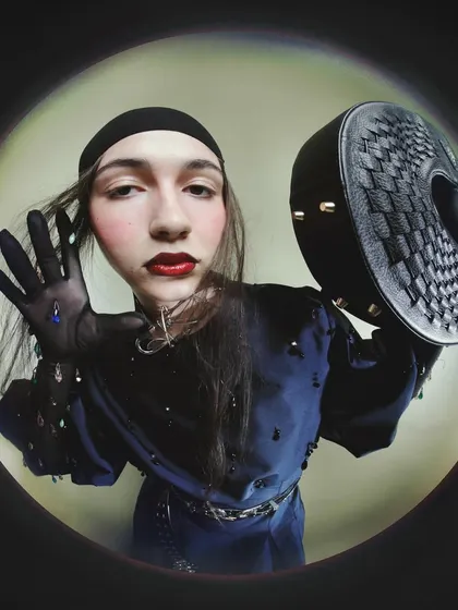 Another fisheye portrait from the 'Peek-a-boo' series, where the model holds a textured black bag. The distorted perspective and direct gaze create an intimate and slightly unnerving connection with the viewer.