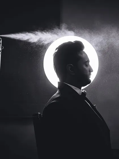 A creative, backlit silhouette of the groom getting his hair styled, captured in dramatic black and white.