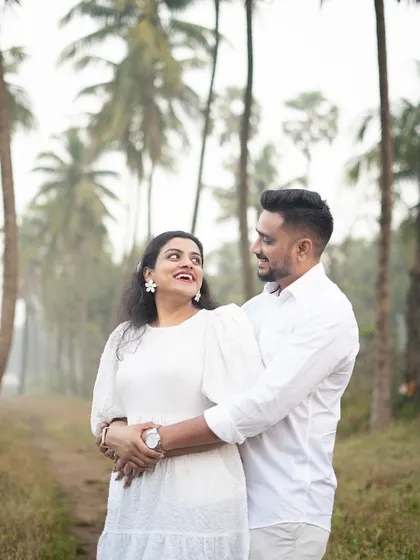 A happy, candid pre-wedding shot of a couple embracing among palm trees. His smile and her joyful expression perfectly capture their love.