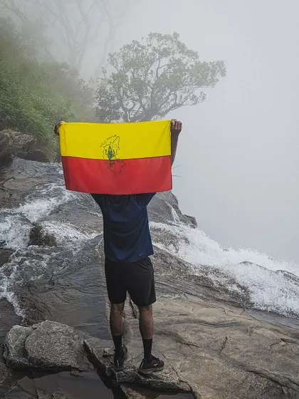 A trekker proudly holds the Kannada flag at the top of Bandaje falls, a moment of pride and natural beauty combined.