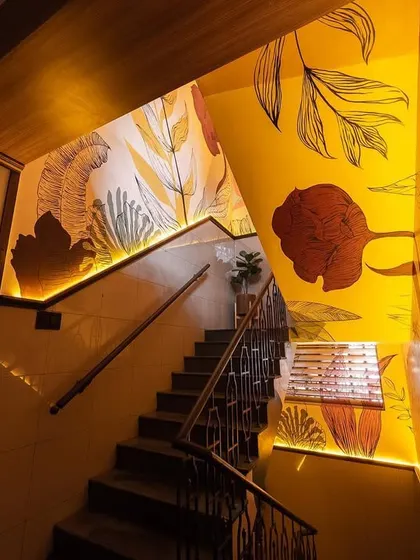 The warm glow of the lighting on the yellow mural creates an inviting and energetic ambiance in this commercial staircase.